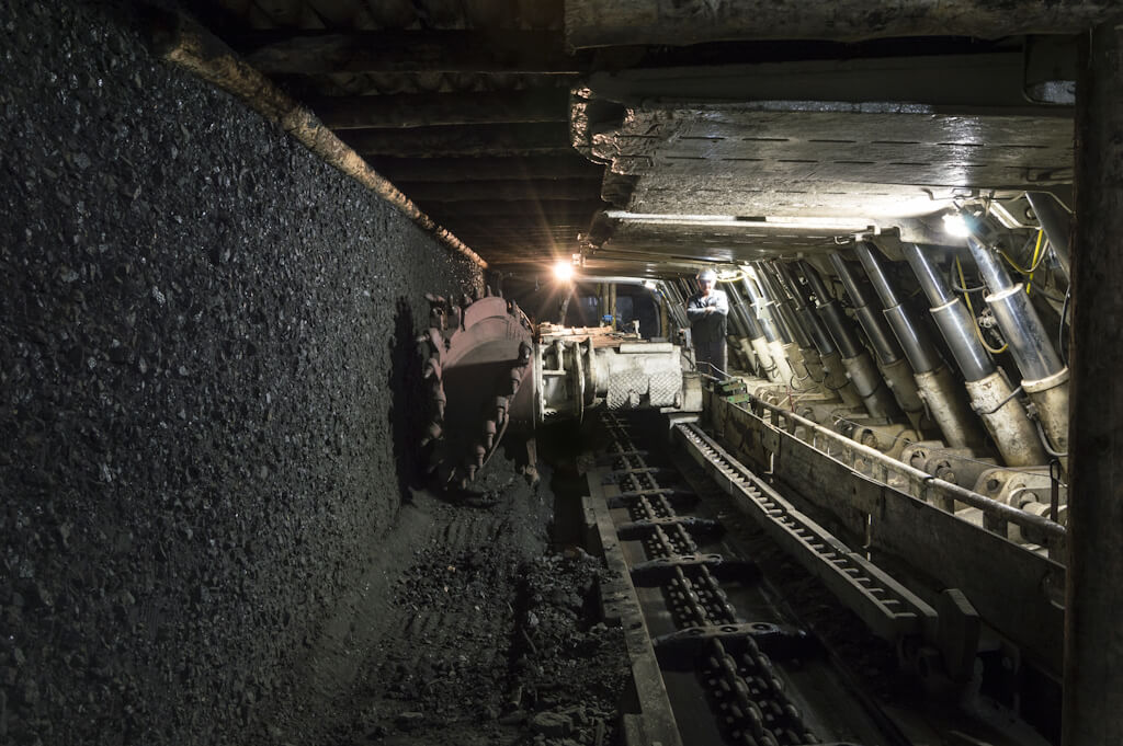 In longwall coal mining, a rotating excavator (left) feeds coal onto a conveyor belt for transport out of the mine. Large hydraulic supports continually advance with the longwall machine, holding up the mine roof to protect both workers and equipment as coal is extracted. As the machine progresses, the conveyor and supports move with it, and the void left behind is allowed to collapse in a controlled manner. Photo: Dreamstime